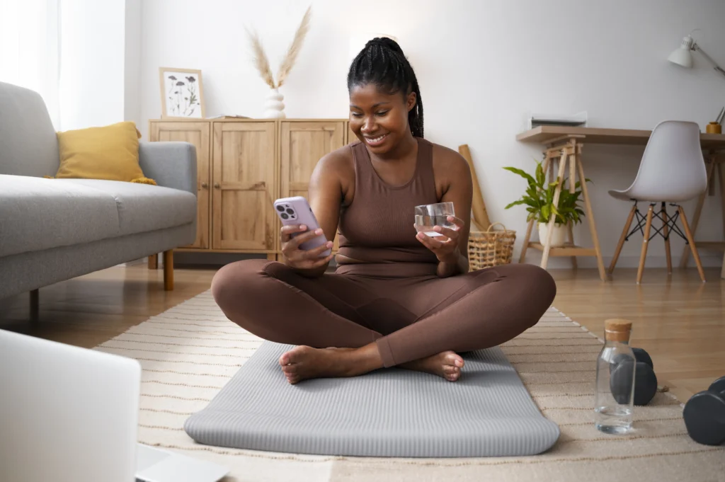 Mulher sentada com o celular em uma mão e na outra um copo com água preparando para iniciar meditação 