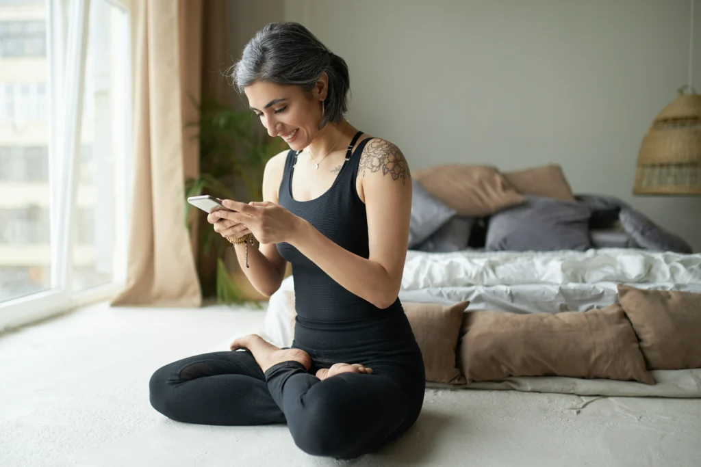 mulher em posição de meditação com celular na mão e vestida de roupa de esporte